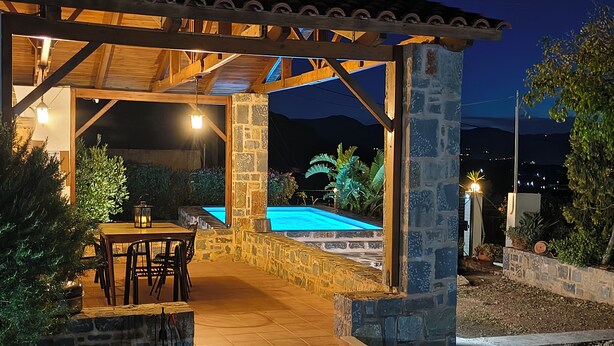 An outdoor patio area with a pool, stone walls, and a pergola structure.