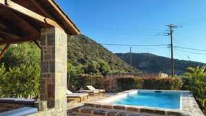 A stone pool with lounge chairs, a stone wall, and a view of a mountain.
