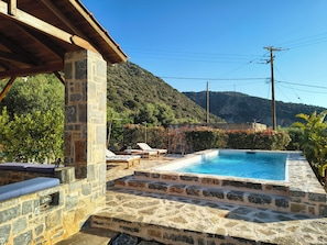 Una piscina de piedra con sillones de descanso, un muro de piedra y vistas a la montaña.