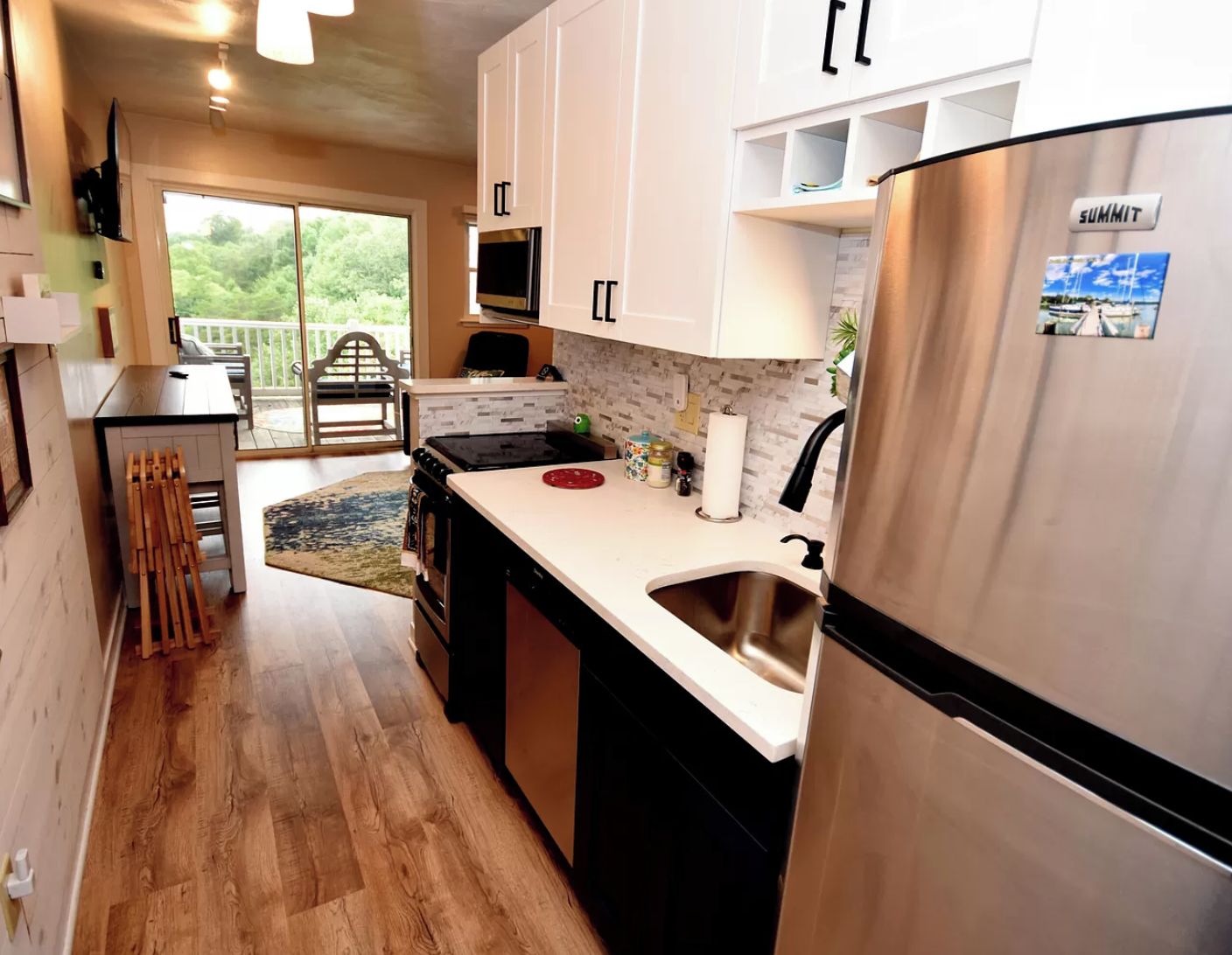 A modern kitchen with white cabinets, a stainless steel refrigerator, and a large window overlooking greenery.