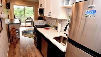 A modern kitchen with white cabinets, a stainless steel refrigerator, and a large window overlooking greenery.