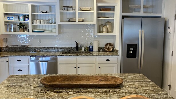 A kitchen with white cabinets, a granite countertop, a stainless steel refrigerator, and three wooden chairs. - Beautiful Reelfoot Lake (Tiptonville)