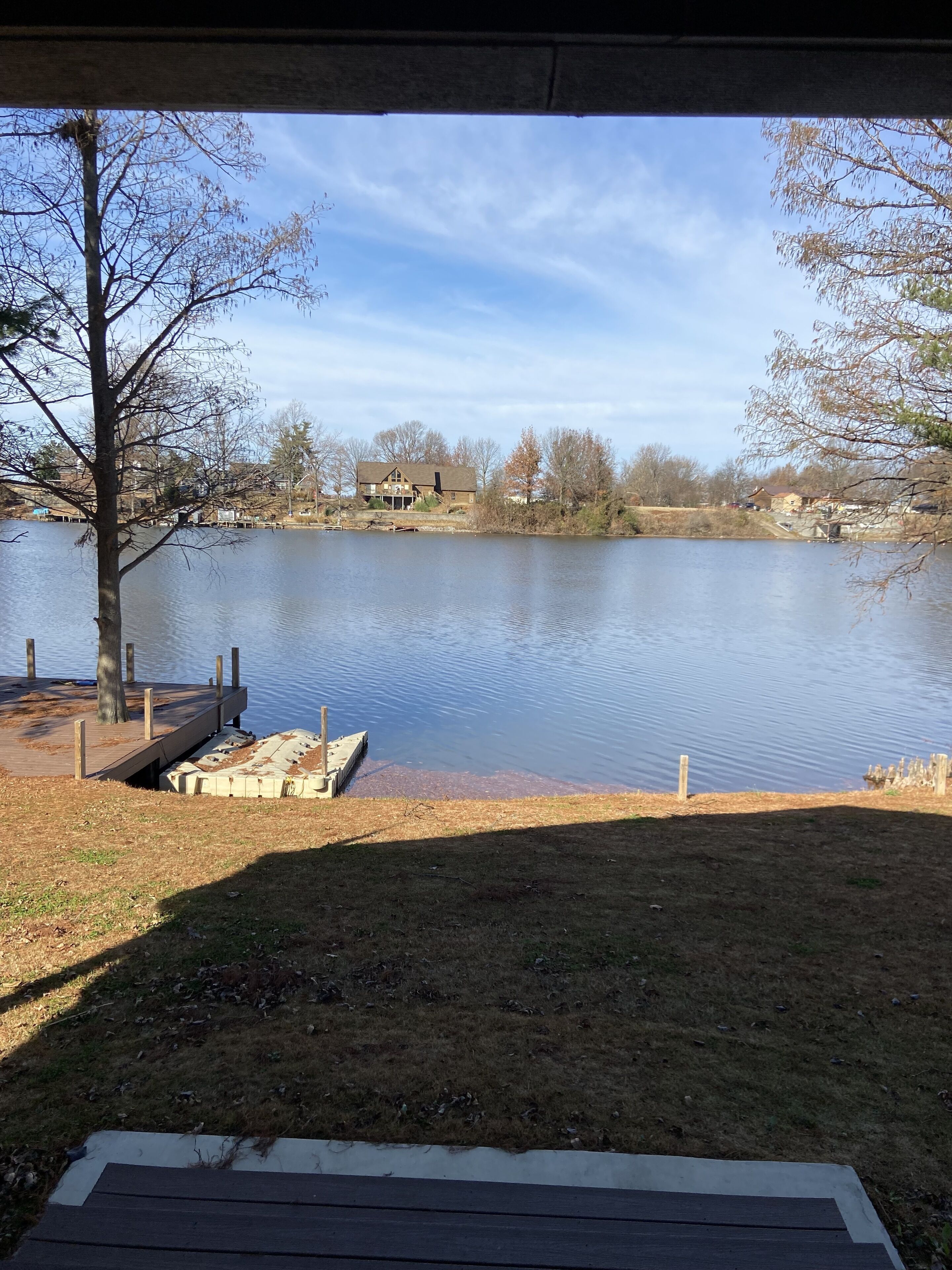 A lakeside view with a dock, grassy area, and houses in the background.