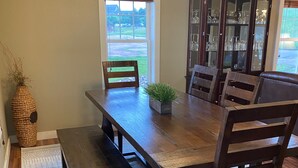 Ein Esszimmer mit Holztisch, Bänken und Stühlen. Über dem Tisch hängt eine Chandelier, und im Hintergrund steht ein Schrank mit Glastüren.