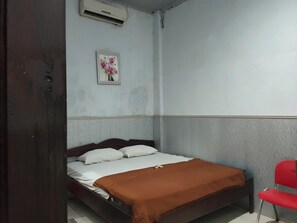 A single bed with a brown blanket, a red chair, and a wall-mounted air conditioner.