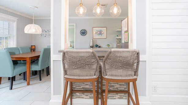 Een eetgedeelte met een houten tafel en groene stoelen, een keuken met witte kasten en een hanglamp boven het aanrecht.
