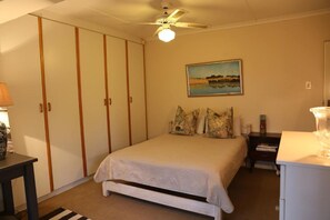 A bedroom with a bed, a nightstand, a lamp, a painting on the wall, and a ceiling fan.