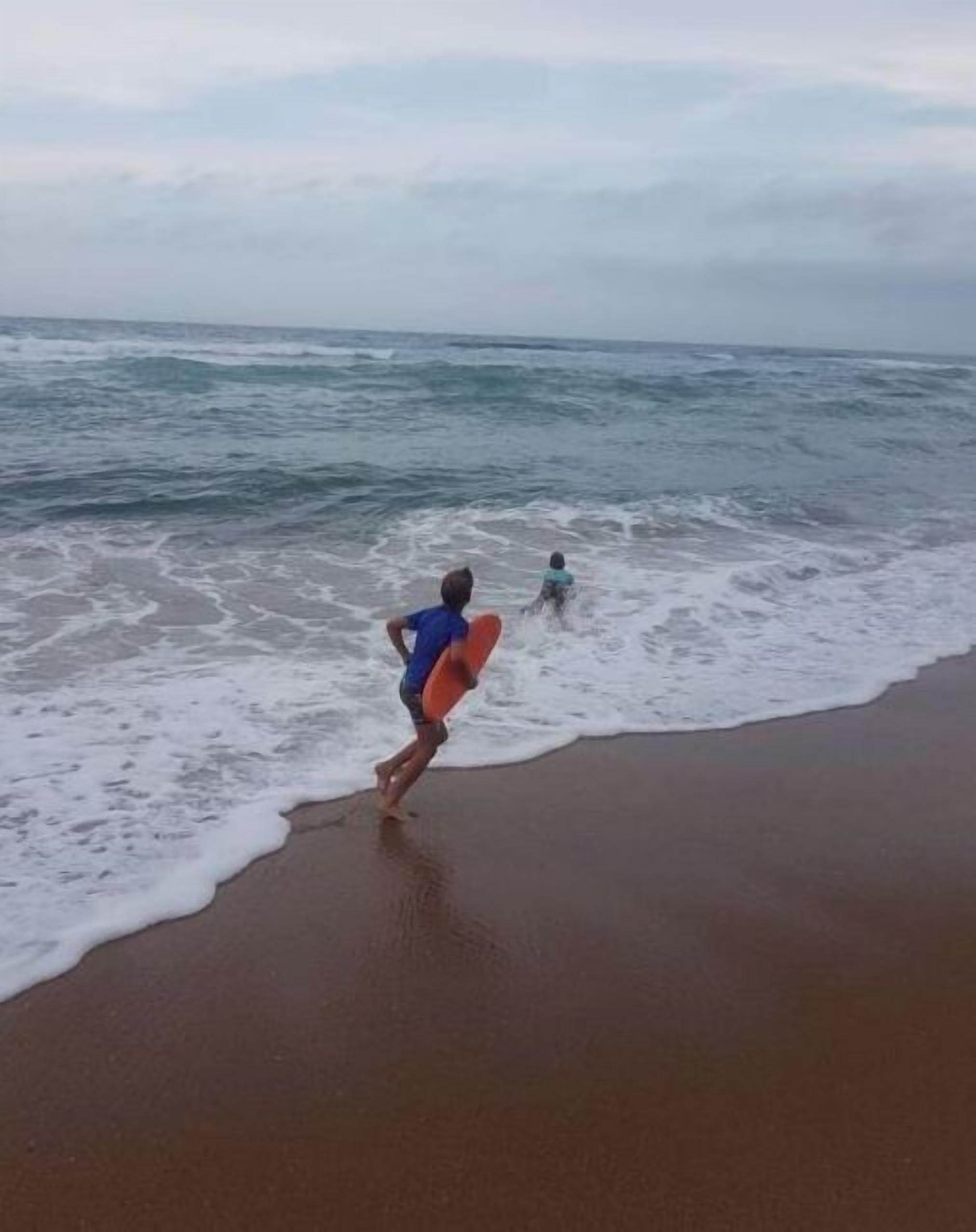 A beach scene with a person running towards the water with a surfboard.