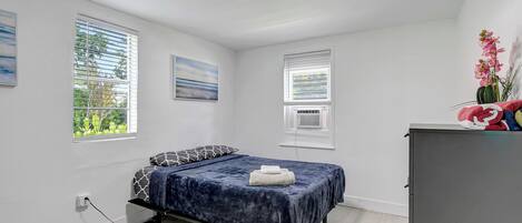 A bedroom with a bed, a desk, and a window with blinds.