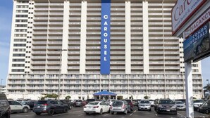 Un grand hôtel avec une enseigne bien visible indiquant « CAROUSEL », de nombreux balcons et un parking où sont stationnées plusieurs voitures.
