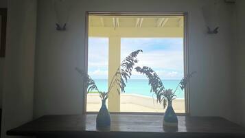 Une pièce dotée d’une grande fenêtre donnant sur une plage, d’une table en bois et de deux vases posés sur la table.