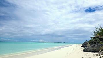 A beach with clear turquoise water, white sand, and rocky outcrops.