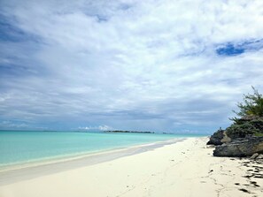 Una playa con agua turquesa cristalina, arena blanca y afloramientos rocosos.