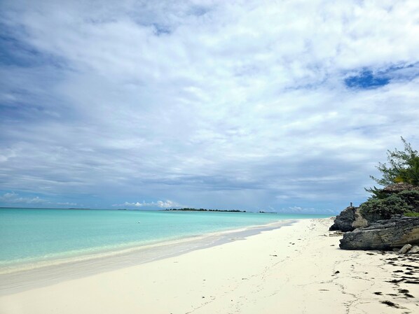 A beach with clear turquoise water, white sand, and rocky outcrops.