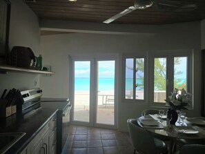 A kitchen with a view of the beach through glass doors, a dining area with a table set for two, and a ceiling fan.