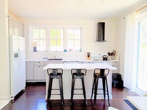 A modern kitchen with a central island, bar stools, a stove, and a window with a view.