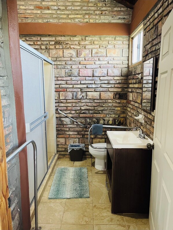 Un baño pequeño con pared de piedra, inodoro, lavabo y una alfombra pequeña.