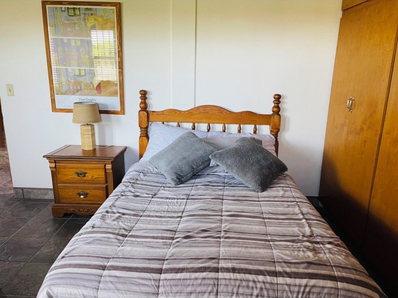 Une chambre à coucher avec un lit en bois, une table de chevet avec une lampe et un tableau encadré au mur.