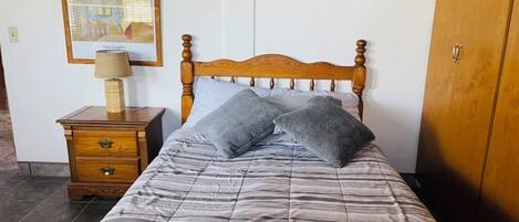 Une chambre à coucher avec un lit en bois, une table de chevet avec une lampe et un tableau encadré au mur.