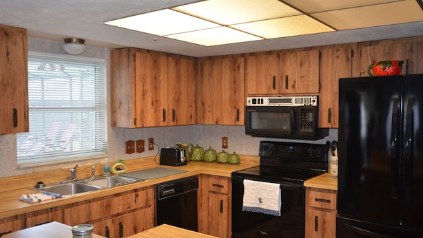 A kitchen with wooden cabinets, a black refrigerator, a microwave, a stove, and a sink.
