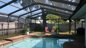 A covered outdoor swimming pool with a hot tub, surrounded by a wooden fence and potted plants.