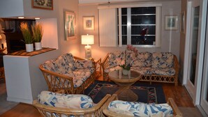 A cozy living room with wicker furniture, a fireplace, and a window with a view of the outside.