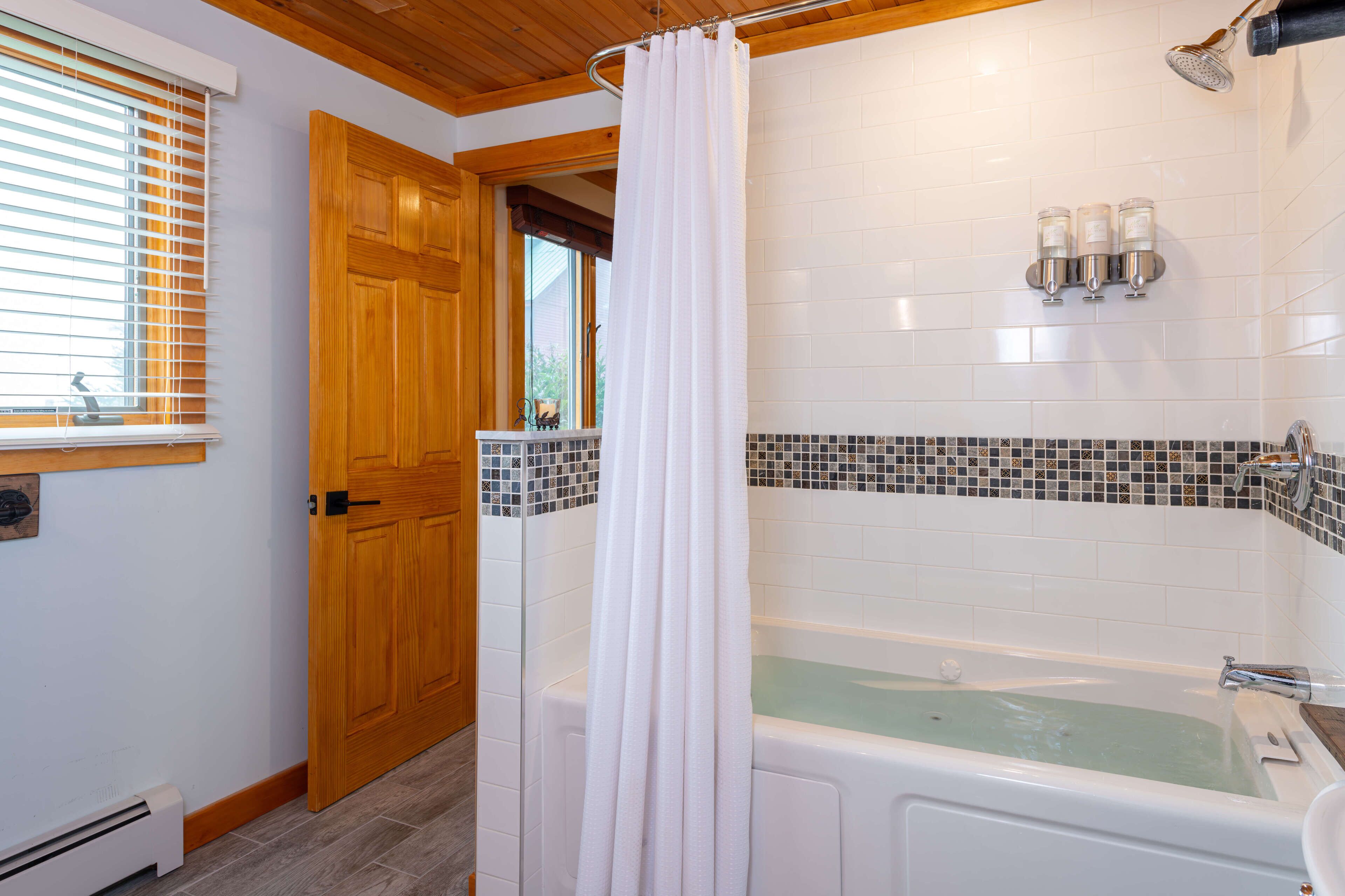 A bathroom with a bathtub, a shower curtain, and a window with blinds.