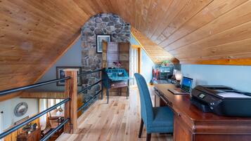 A cozy attic room with wooden beams, a stone wall, a desk with a laptop, and a printer.