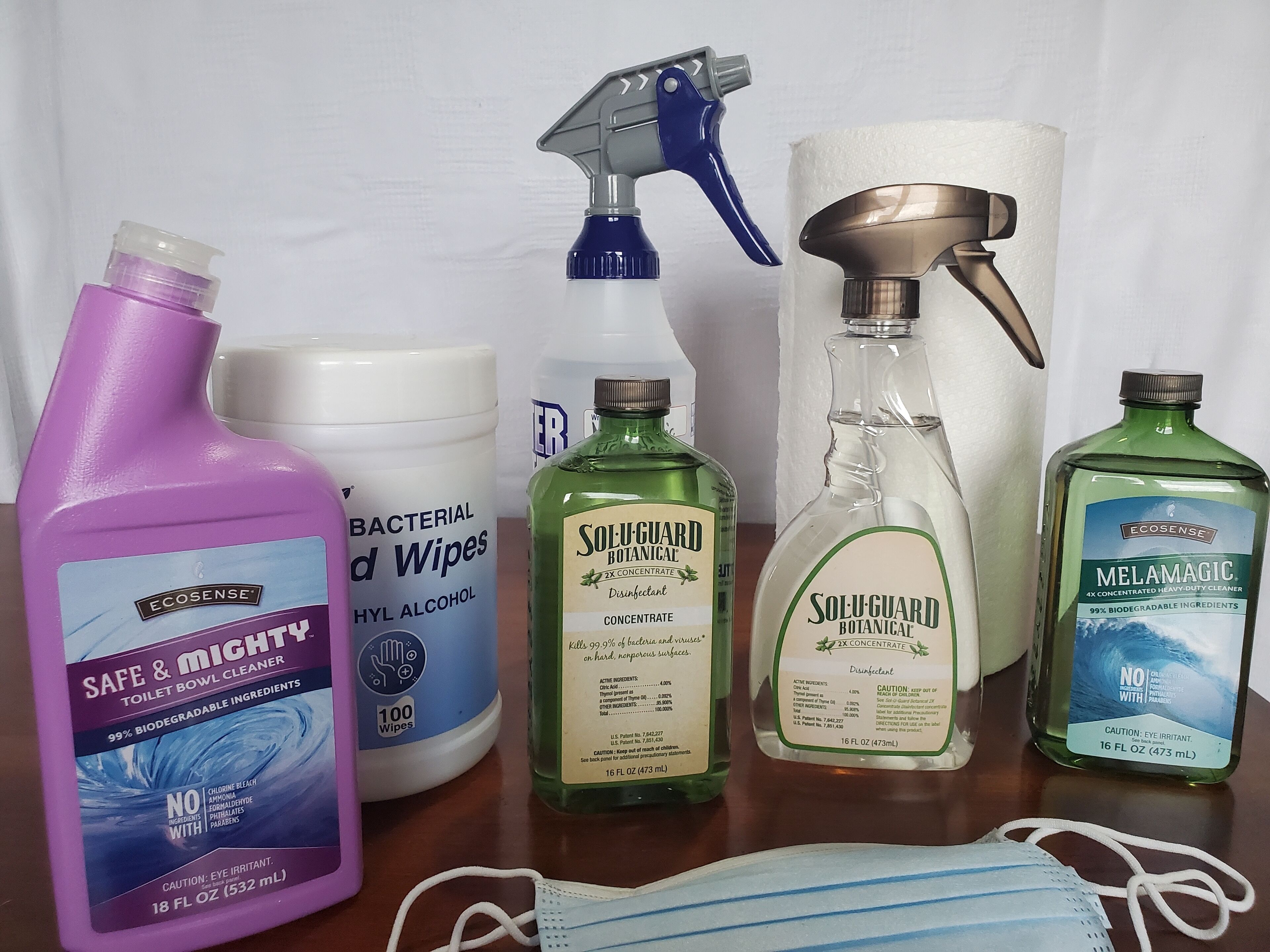 A variety of cleaning supplies including a bottle of toilet bowl cleaner, a spray bottle, a bottle of hand sanitizer, and a face mask.