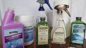 A variety of cleaning supplies including a bottle of toilet bowl cleaner, a spray bottle, a bottle of hand sanitizer, and a face mask.