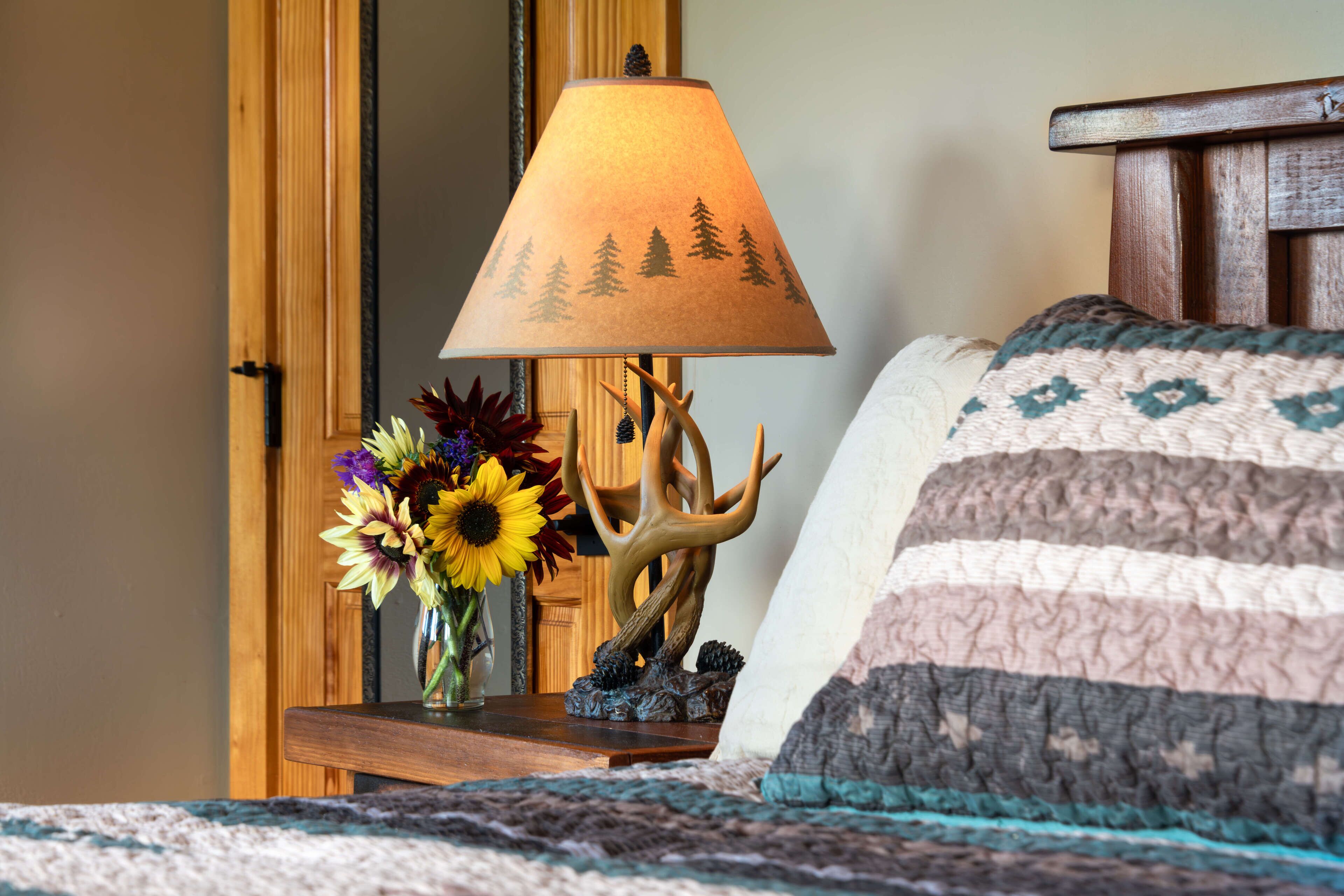 A bed with a striped pillow and a lamp with a tree design on the table beside it.
