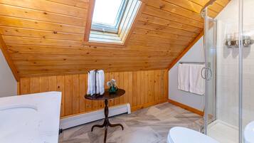 Un bagno con rivestimenti in legno, un lucernario, cabina doccia in vetro e un piccolo tavolo con asciugamani.
