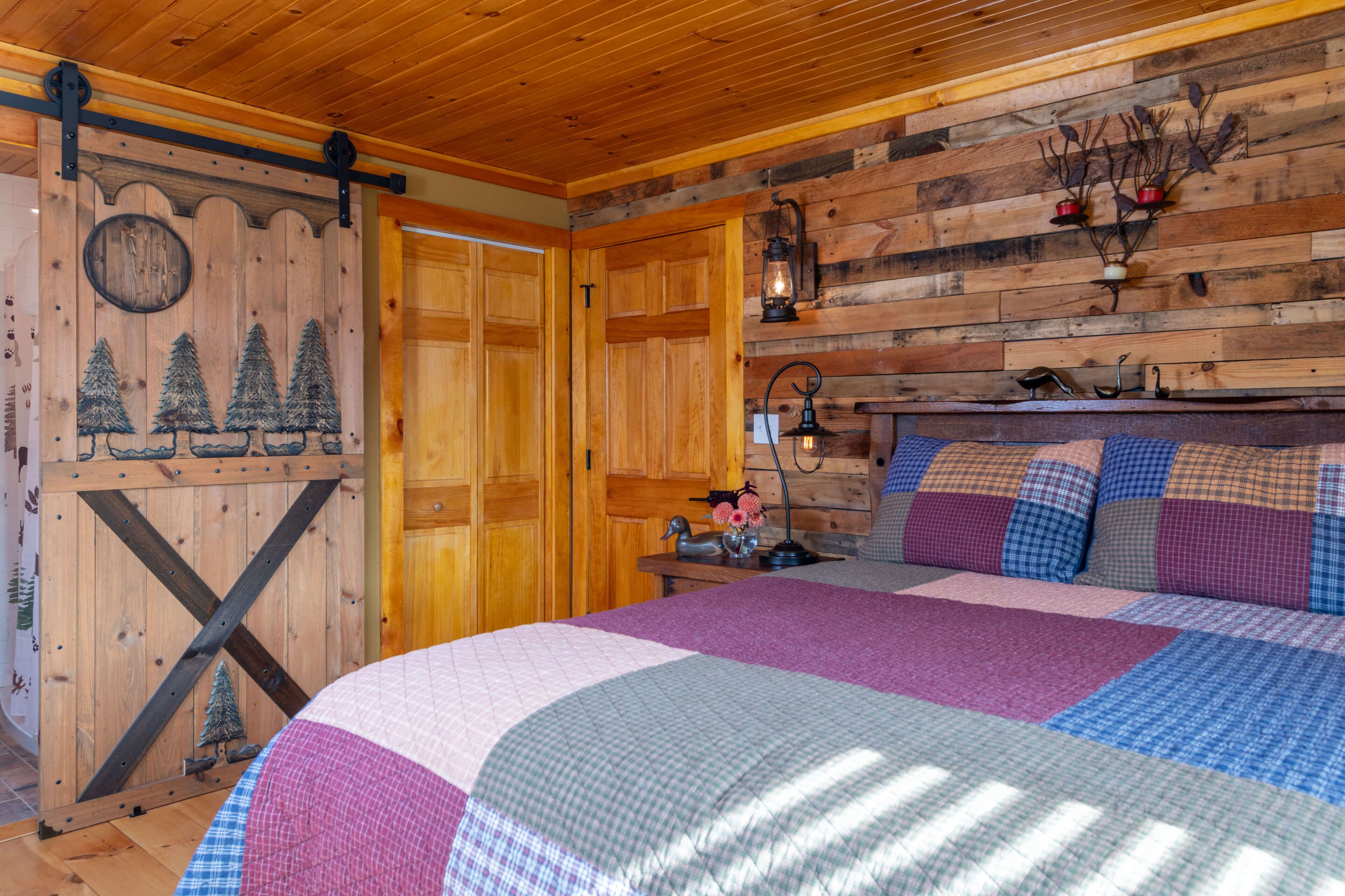 Una habitación acogedora con techo de madera, una cama con colcha, un aparador y una lámpara de pared.