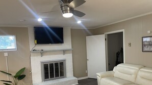 Un salon avec une cheminée, un canapé, une table basse, un ventilateur de plafond et un téléviseur fixé au mur.