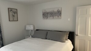 Une chambre à coucher avec un lit, une table de chevet avec une lampe, une porte et deux œuvres d’art murales.