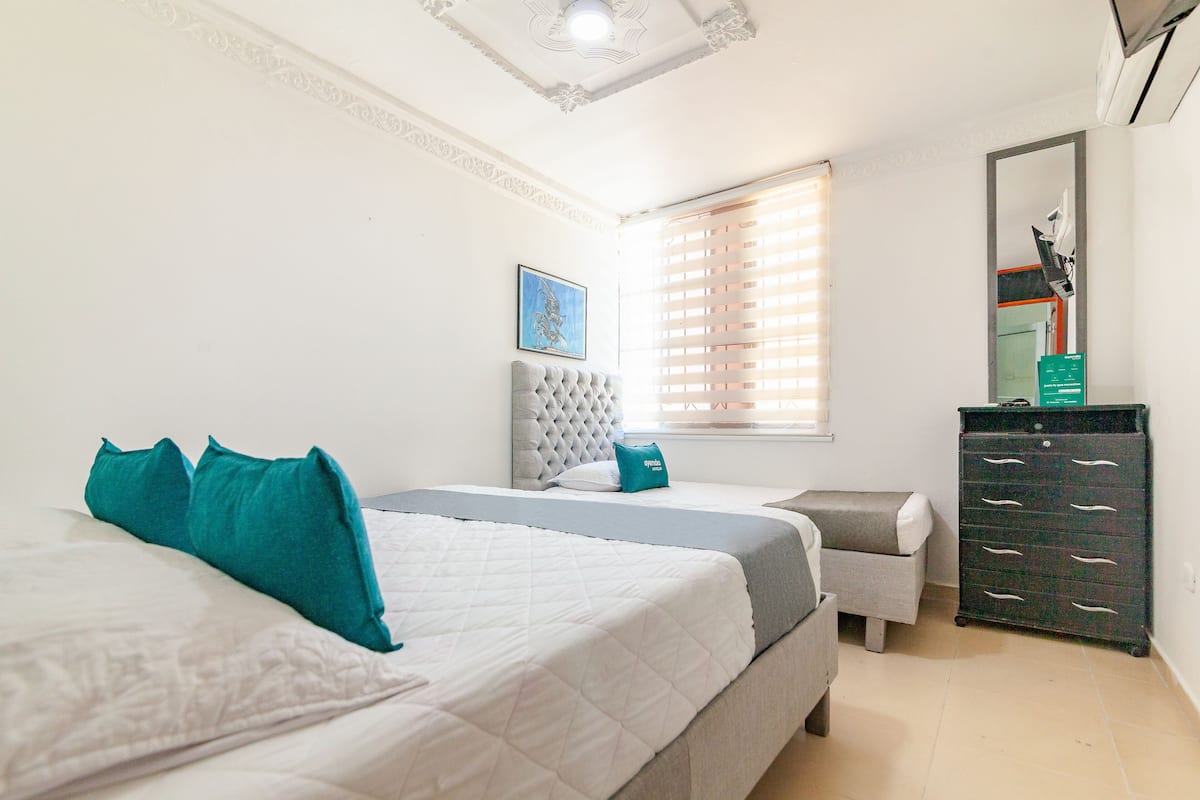 A bedroom with two beds, a dresser, a chair, and a window with blinds.