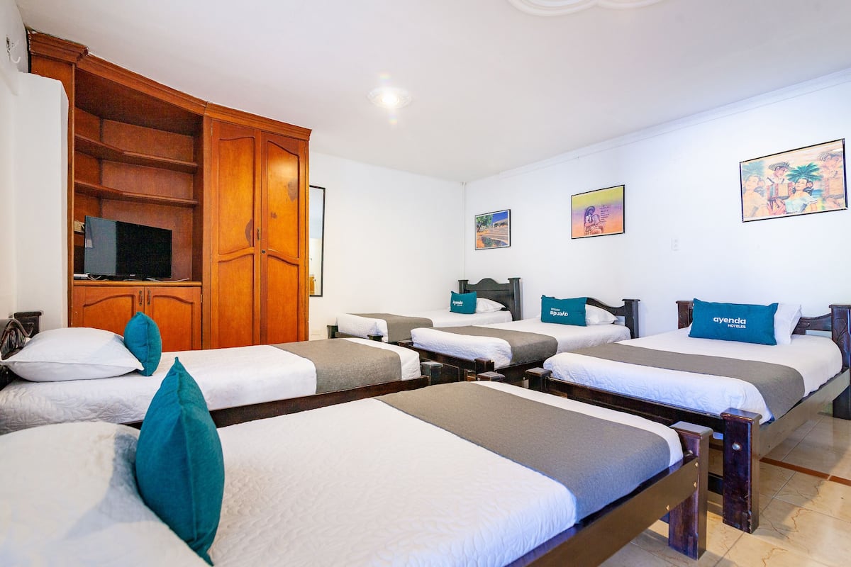 A hotel room with four single beds, a wooden wardrobe, a flat-screen TV, and artwork on the walls.