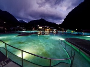 A pool area with clear water, surrounded by mountains and a building with lights.