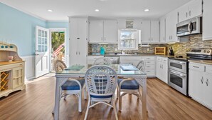 A modern kitchen with white cabinets, a glass dining table, and a wooden floor. - Bogue Sound Cottage with Boat Dock & Pet Friendly (Emerald Isle)