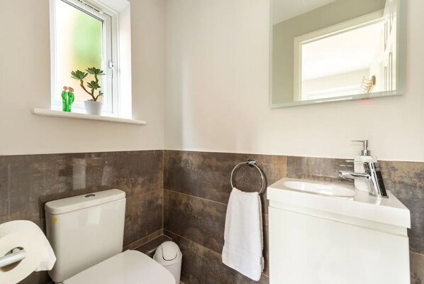 A bathroom with a toilet, sink, and a window with a plant.