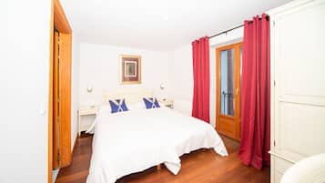 Ein Schlafzimmer mit einem Bett, einem Nachttisch, einem gerahmten Bild an der Wand und roten Vorhängen.