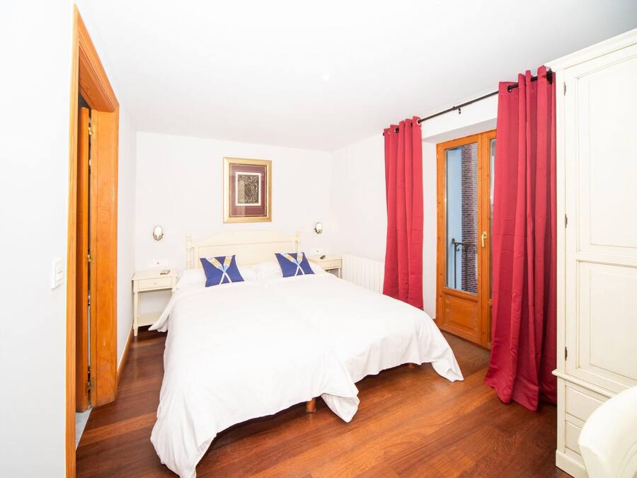A bedroom with a bed, a nightstand, a framed picture on the wall, and red curtains.