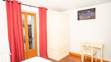 A bedroom with a bed, a wardrobe, a desk with a chair, and a TV on the wall.