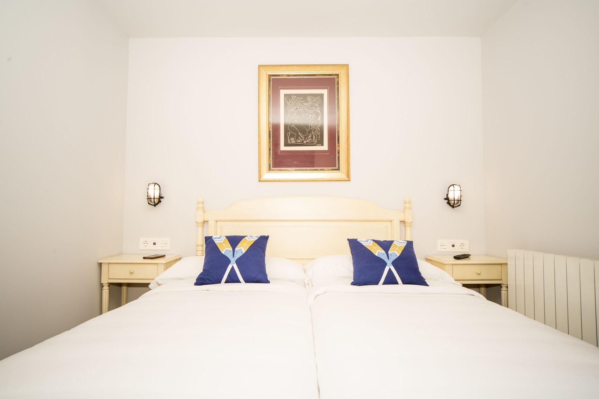 A double bed with two pillows, a nightstand with a lamp, and a framed picture on the wall.