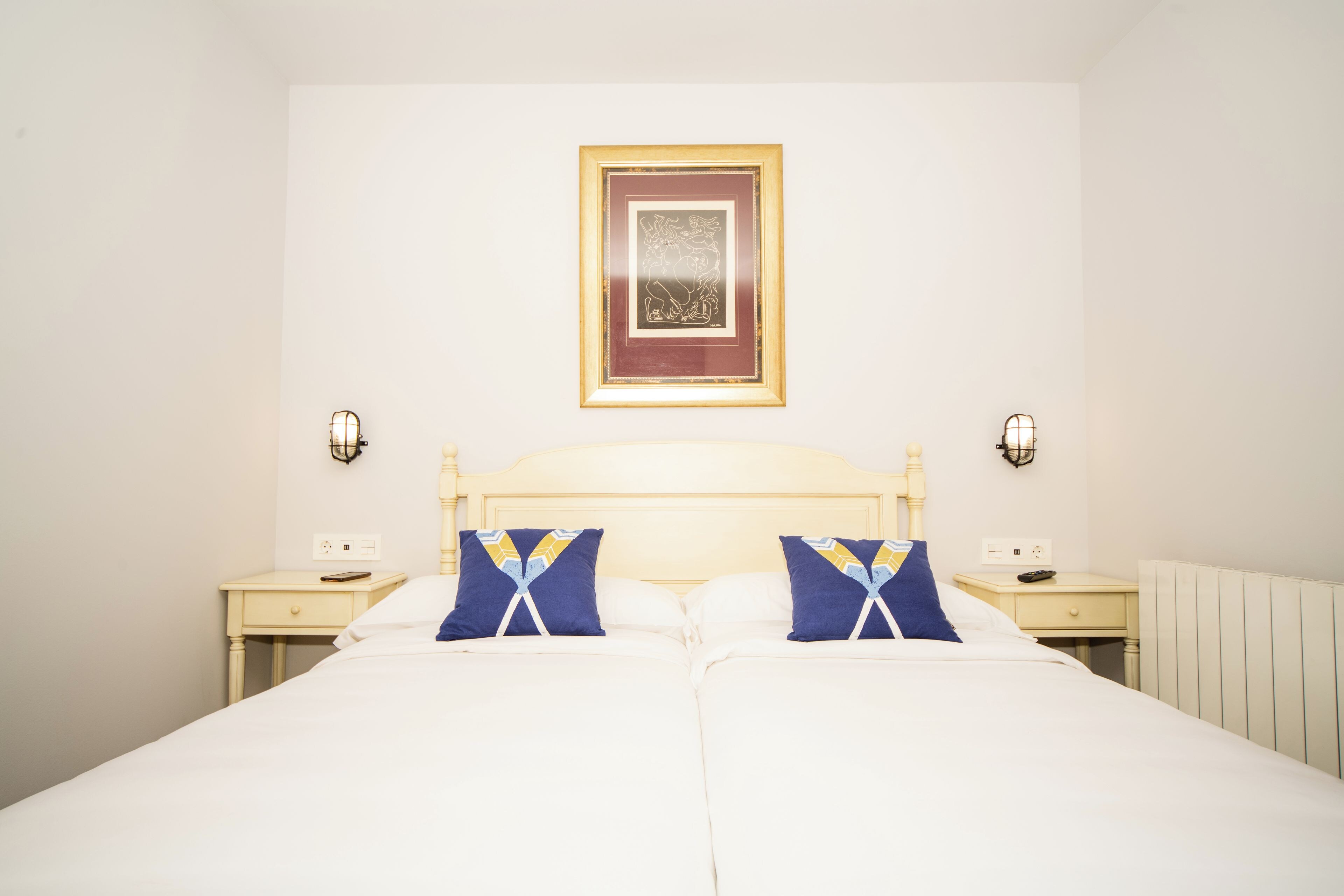 A double bed with white bedding, two bedside tables, and a framed picture on the wall.