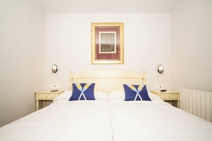 Una cama doble con ropa de cama blanca, dos mesitas de noche y un cuadro enmarcado en la pared.