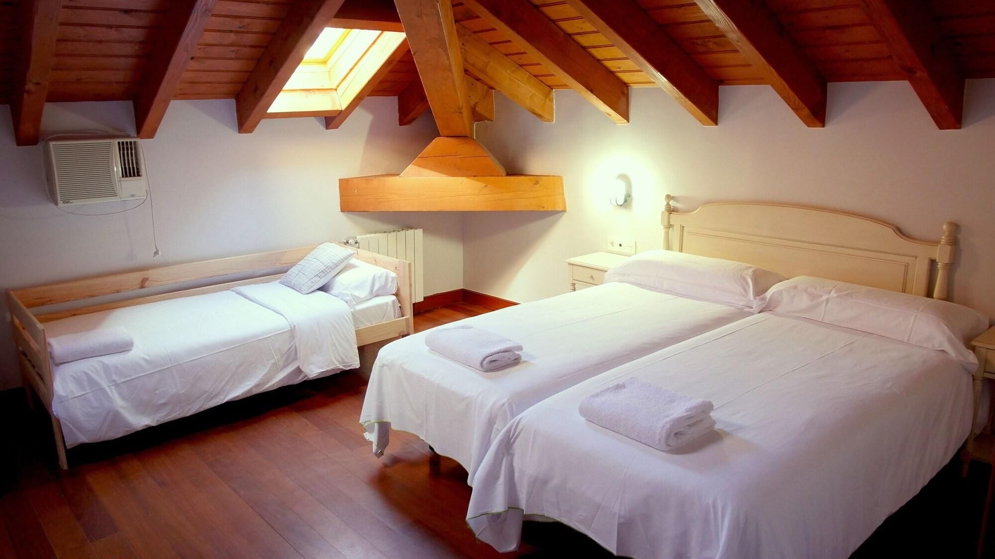 A room with two single beds, a wooden ceiling, and a skylight.