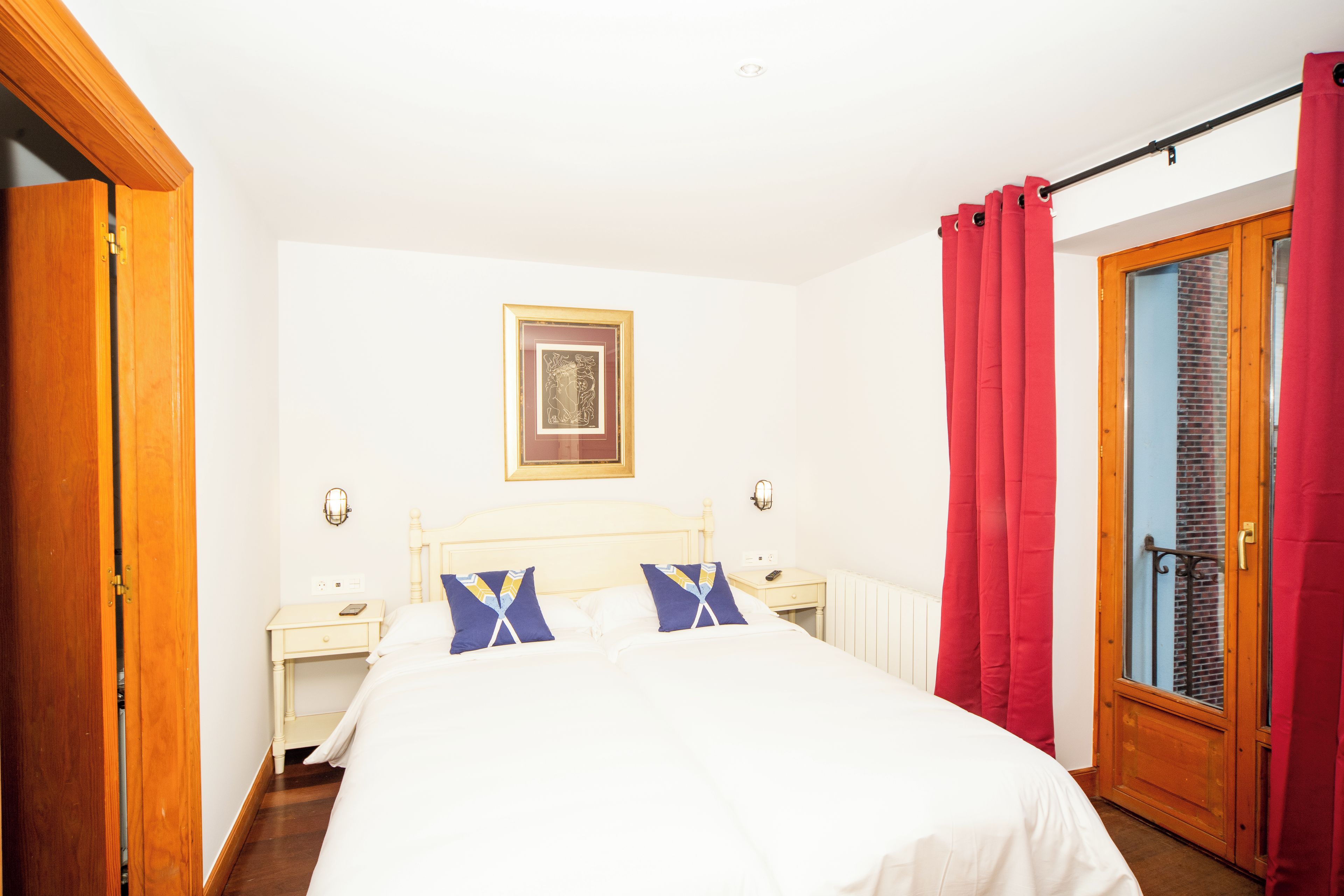 Um quarto com uma cama, mesas de cabeceira, um quadro na parede e uma janela com cortinas.