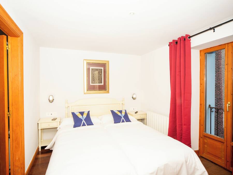 Um quarto com uma cama, mesas de cabeceira, um quadro na parede e uma janela com cortinas.