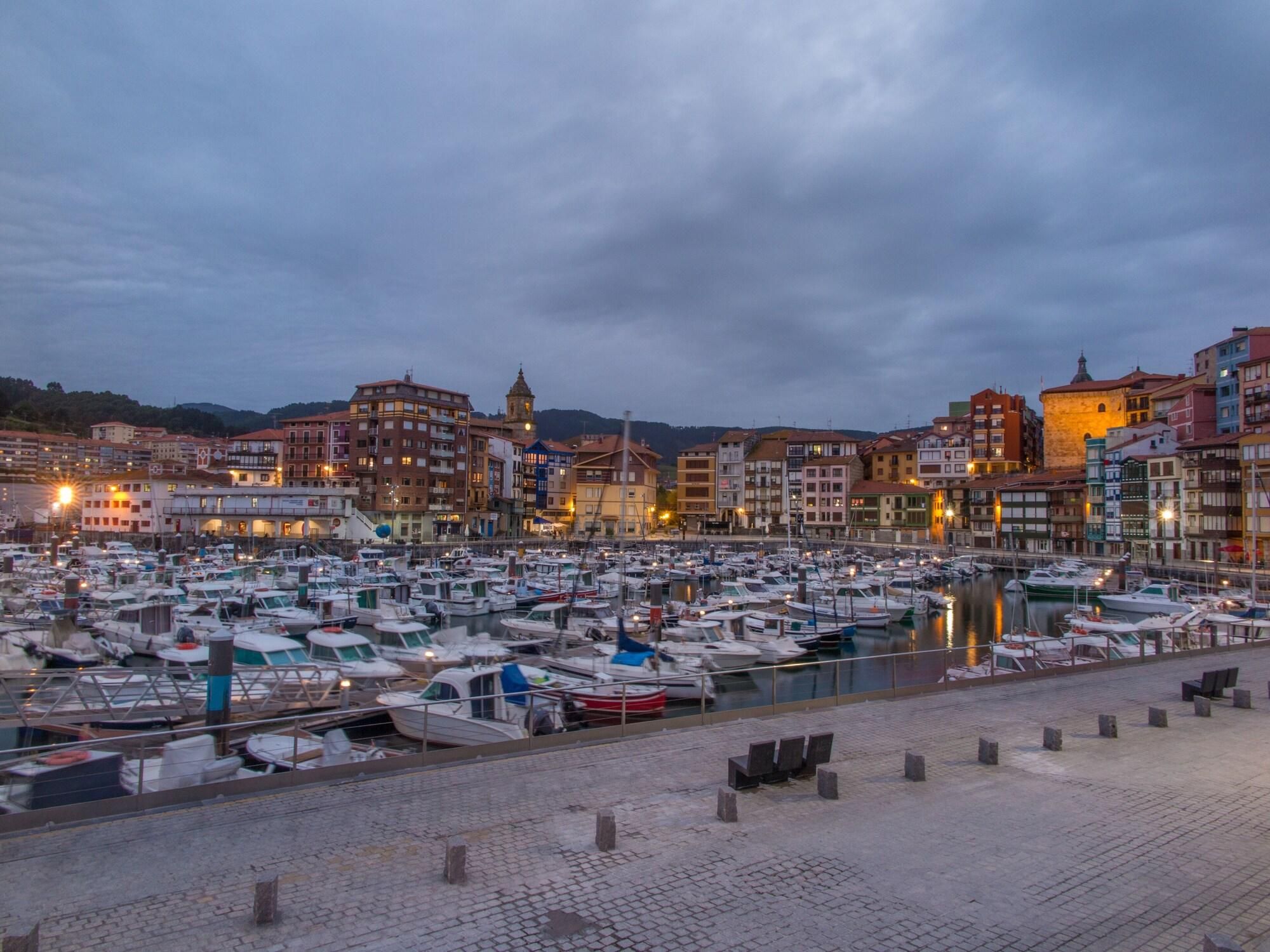 Un puerto deportivo lleno de barcos, rodeado de edificios históricos con una torre destacada.